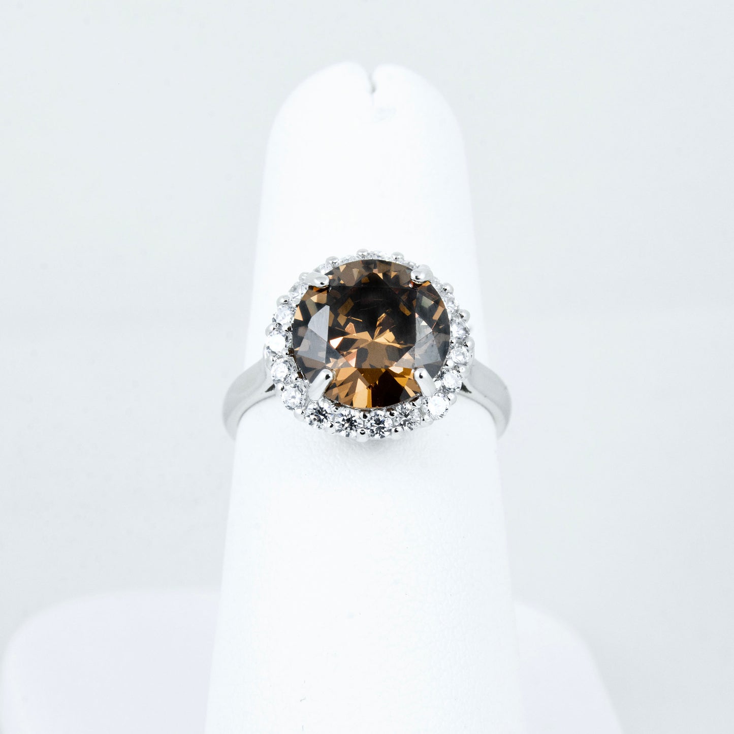 Non-tarnishing, rhodium plated, 925 sterling silver ring. Features a large coffee coloured round-cut centre AAA quality cubic zirconia stone surrounded by a halo of small clear cubic zirconia stones. Centre stone comes in two colours: black and coffee. Available in sizes 5, 6, 7, 8, and 9.